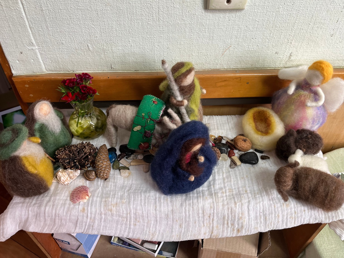 A needle-felted nativity table with Mary, Joseph, shepherds, angels, felted trees, and small natural treasures