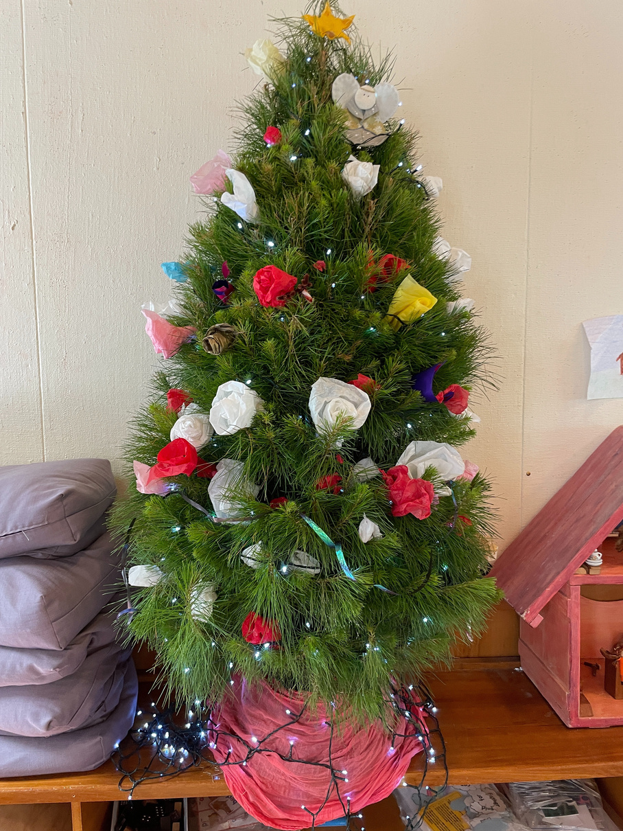 A Christmas tree decorated with tissue paper roses in white, red, pink, and green with fairy lights