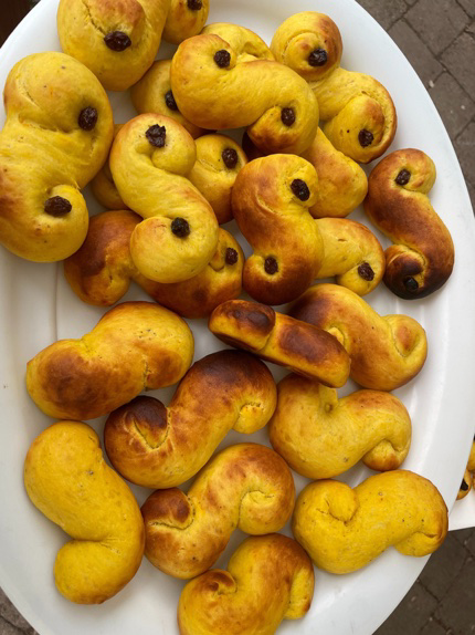 Children shaping small S-shaped St Lucia buns on baking trays in a kitchen