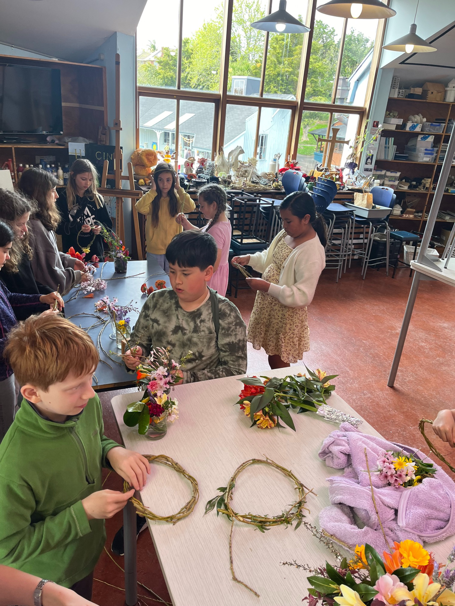 Children gathered around a table making flower crowns from willow and fresh flowers