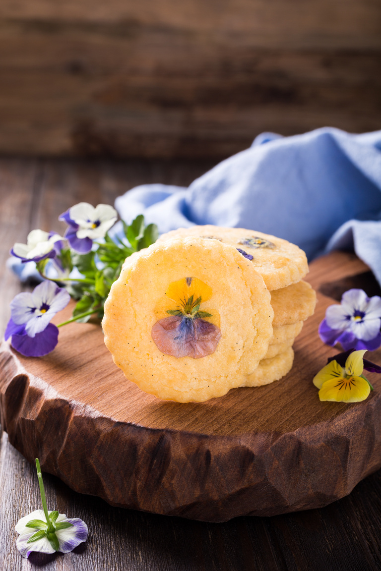 Round shortbread cookies with pressed edible flowers on top, served on a wooden board