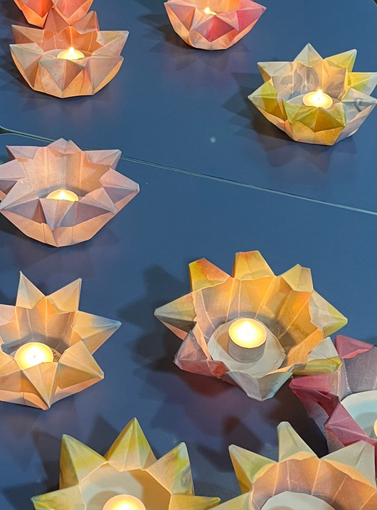Folded paper lanterns glowing warm with tea lights, arranged in rows