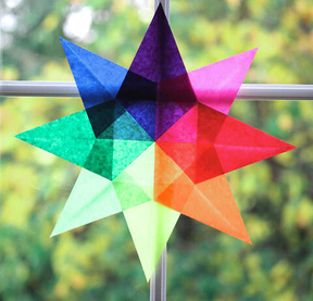 A multi-coloured translucent kite paper window star glowing in a sunny window