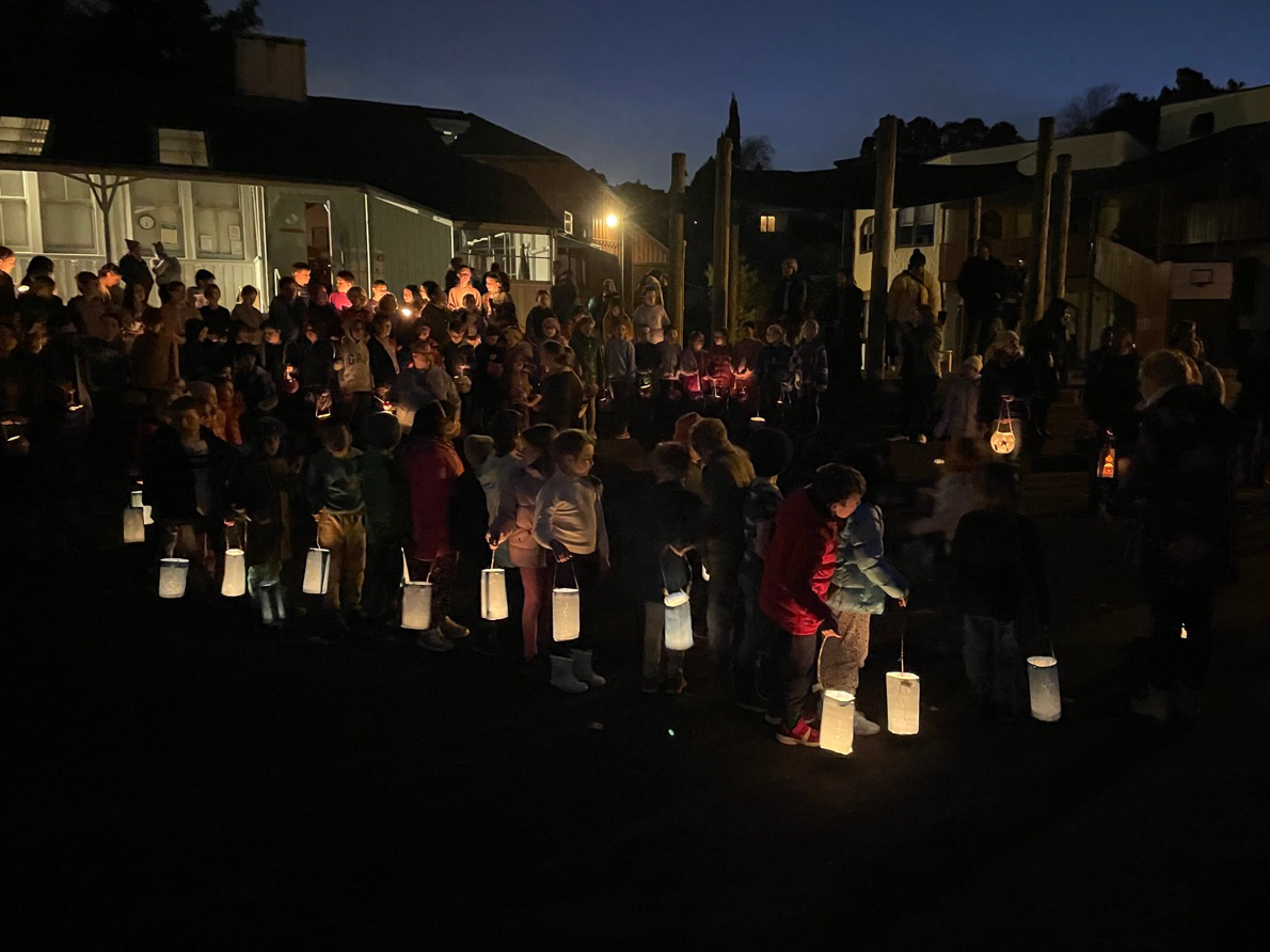 A community lantern walk at dusk, children and families carrying glowing lanterns