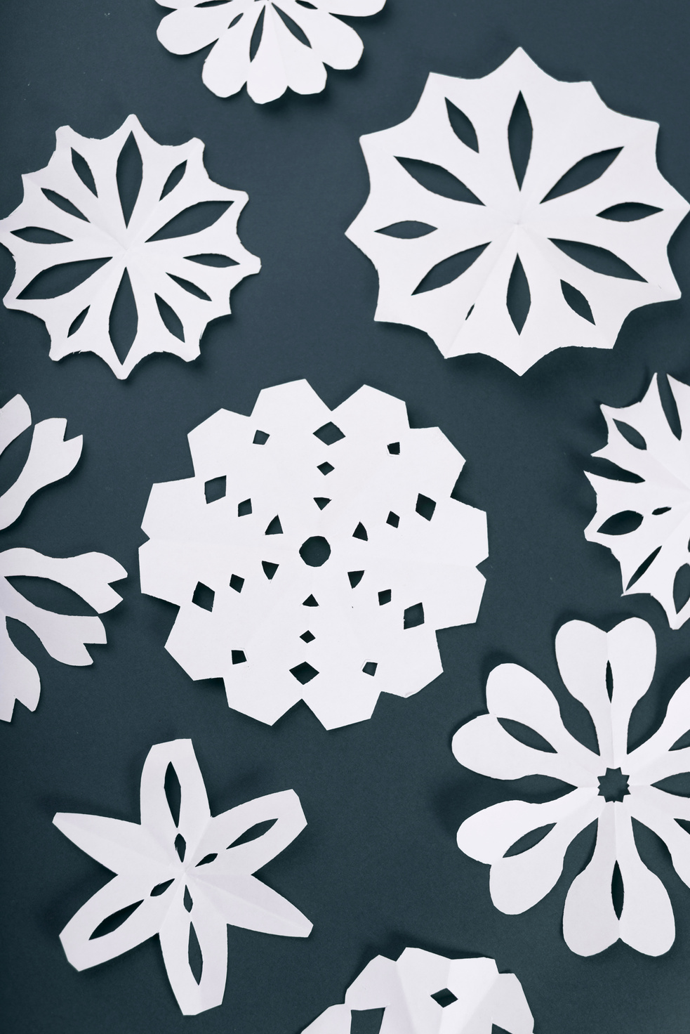 Delicate white paper snowflakes arranged on a dark teal background