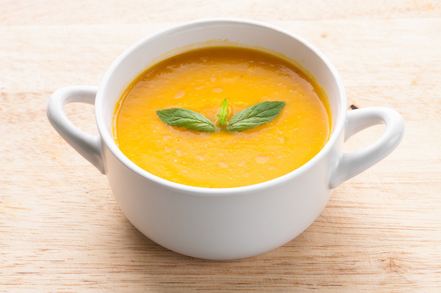 Creamy golden pumpkin soup in a white mug, garnished with fresh basil