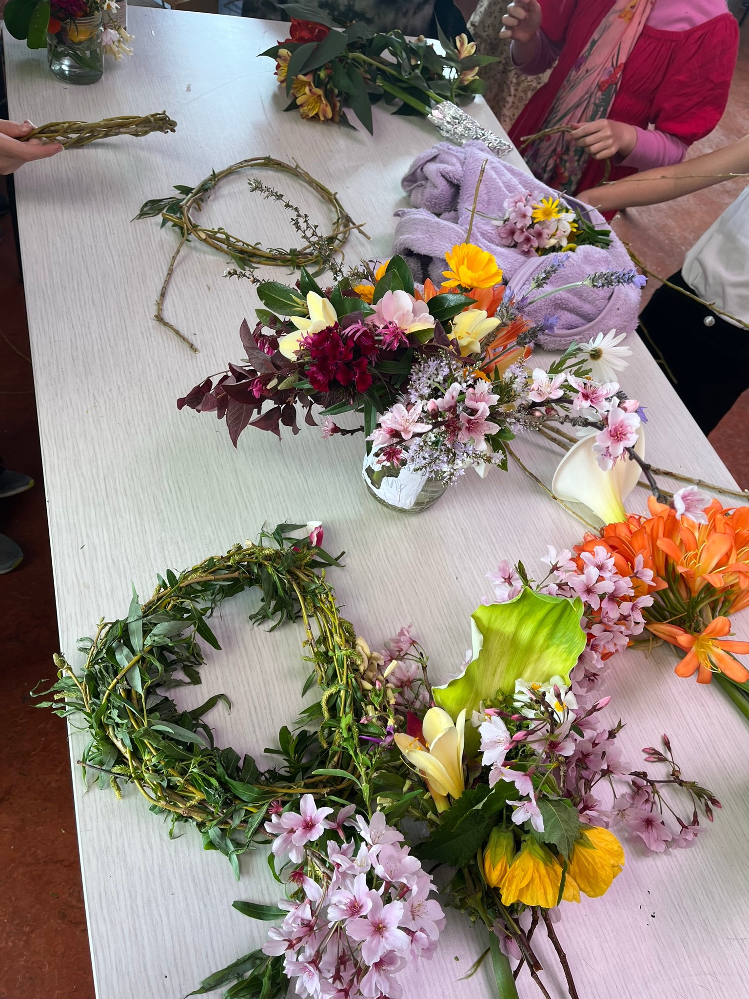 Fresh flowers, willow rings, and leaves laid out on a table ready for flower crown weaving